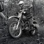 Motorcyclist racing through forest trail in competition.