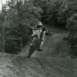 Motorcyclist performing wheelie on dirt track.