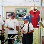 Men displaying motorcycle memorabilia at outdoor event.