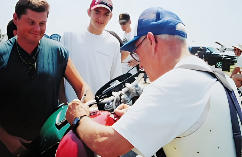 Man signing motorcycle tank at event.