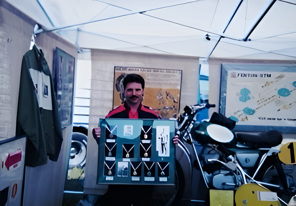 Man displaying medals and motorcycle in exhibition tent.