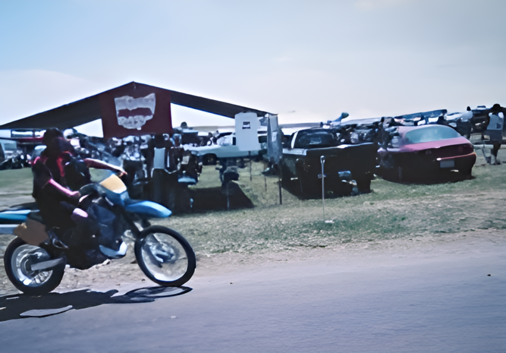 Motorcyclist rides past an outdoor car show.