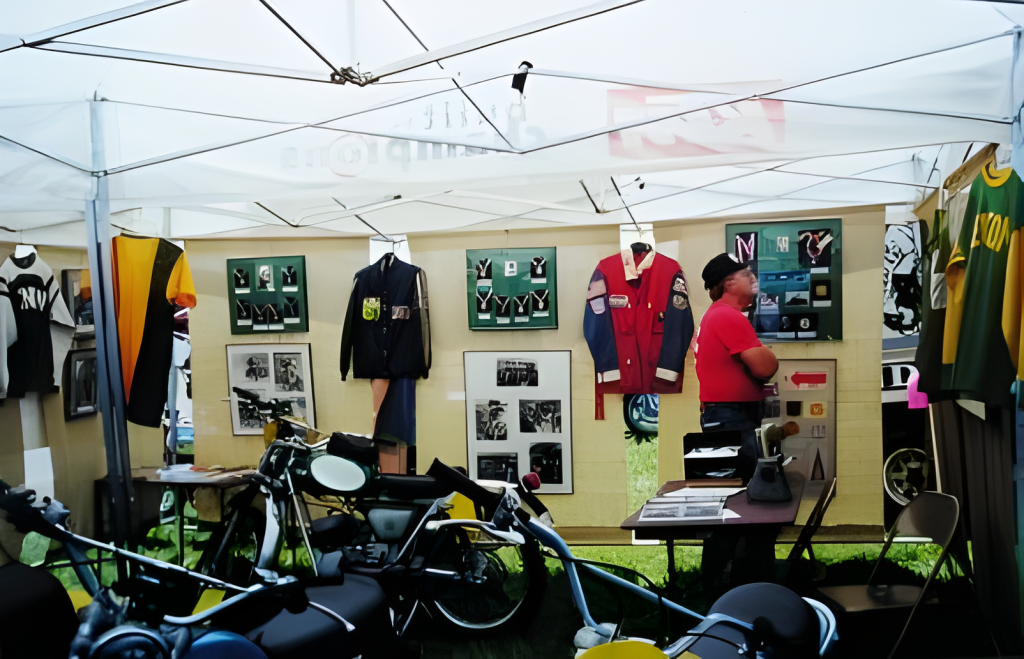 Man in memorabilia tent with vintage motorcycles.