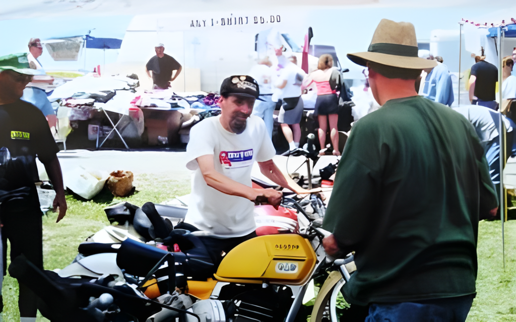 Man displaying motorcycle at outdoor market event.