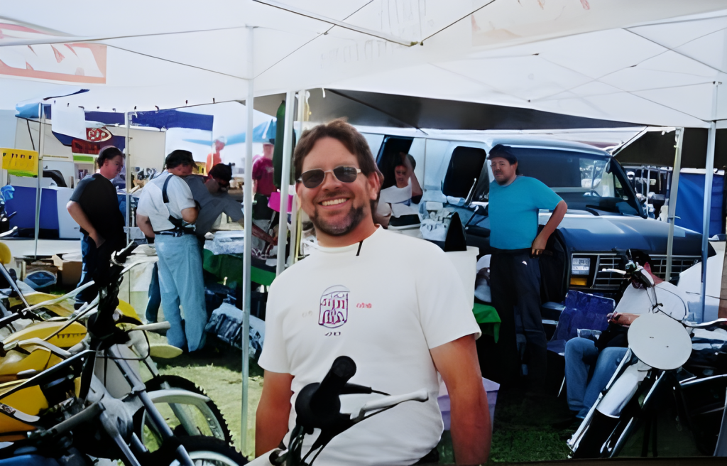 Man smiling at motorcycle event under tent.