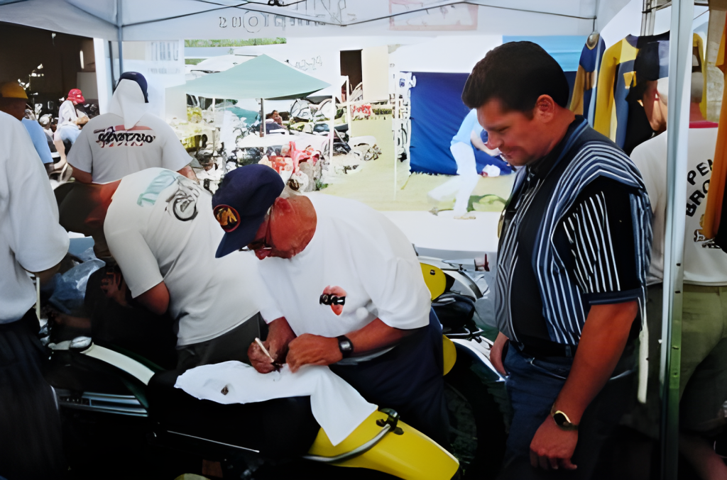 Man signing shirt, surrounded by motorcycles.