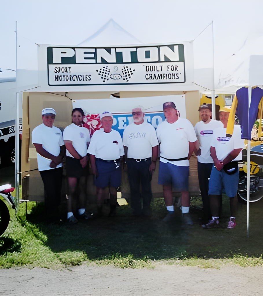 Group in front of Penton motorcycle sign at event.