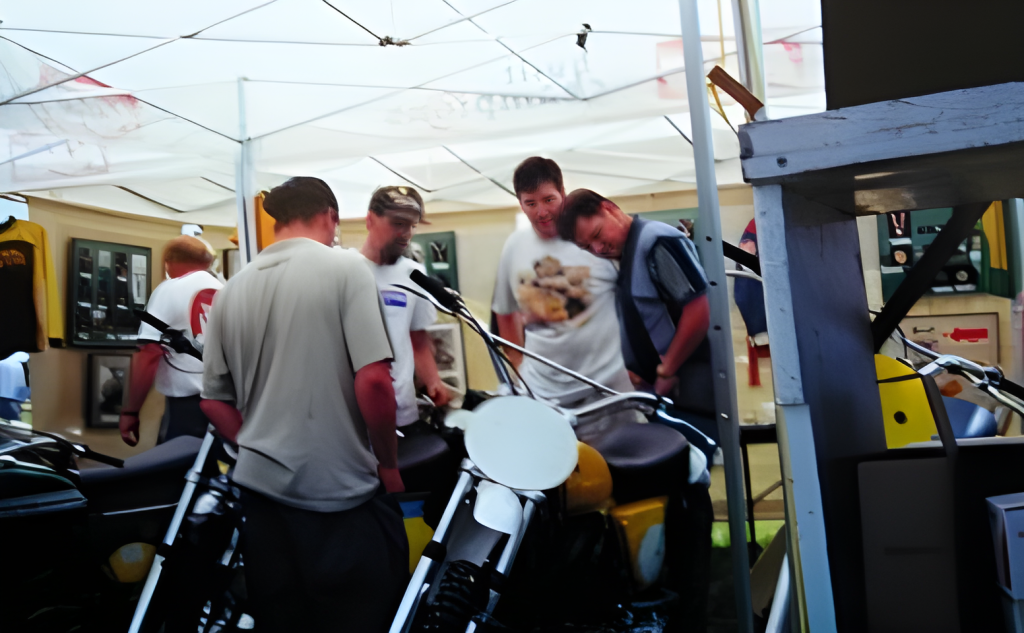 Men examining vintage motorcycles under a tent.