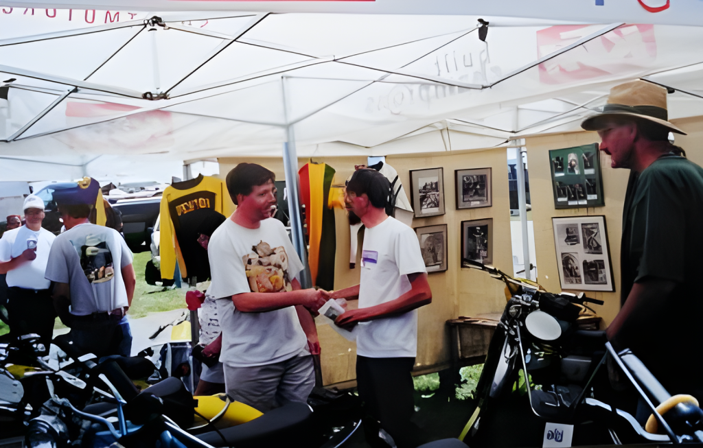 People shaking hands at motorcycle event booth.
