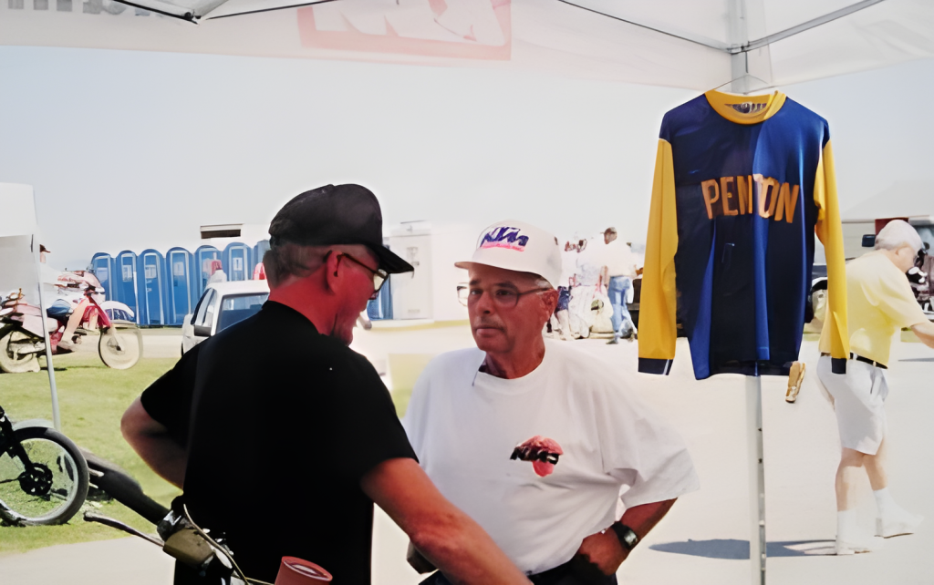 Two men discussing vintage motorcycle gear at outdoor event.