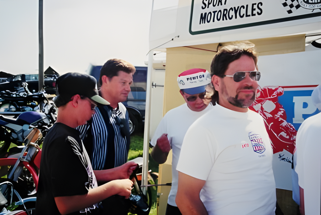 Group at motorcycle event with bikes and signage.