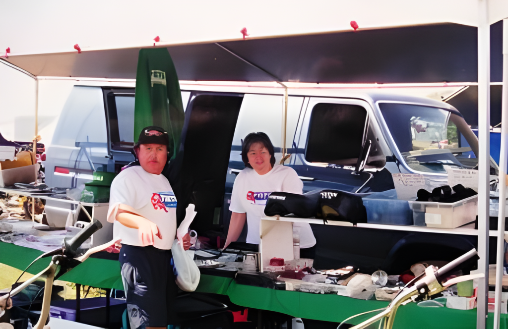 Two people at outdoor market booth with van.