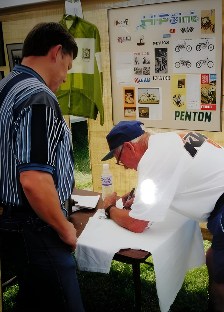 Two men at a vintage motorcycle exhibition table.