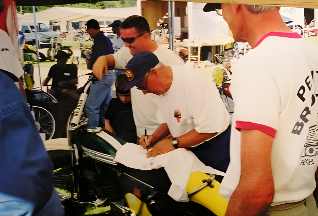 Man signing autographs at vintage motorcycle event.