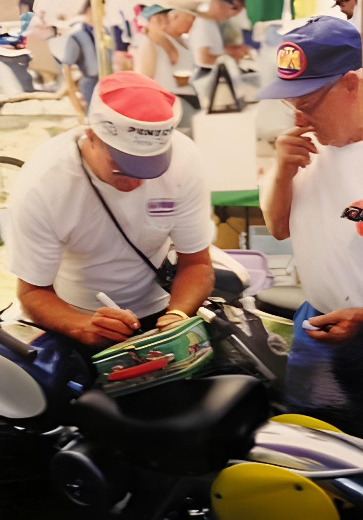 Man signing helmet at outdoor event.