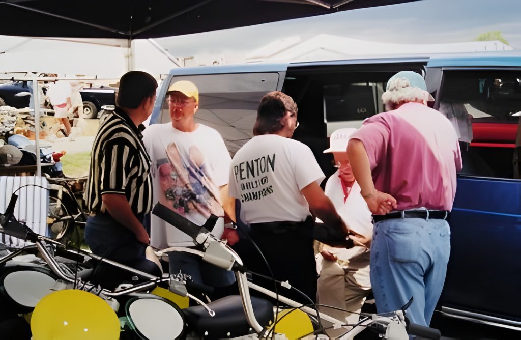 Group discussing near vintage motorcycles at outdoor event.