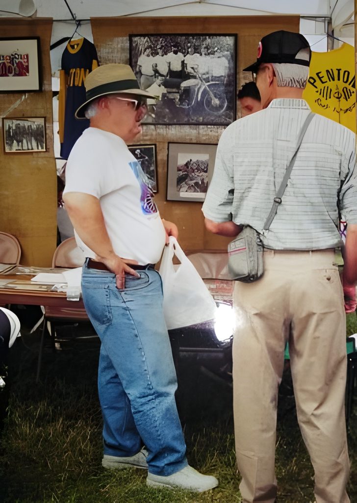 Men conversing at vintage motorcycle exhibit tent.