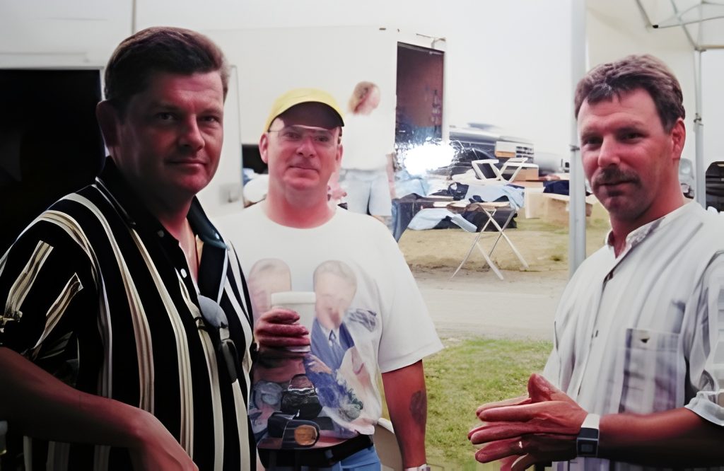 Three men posing outdoors, dressed casually.