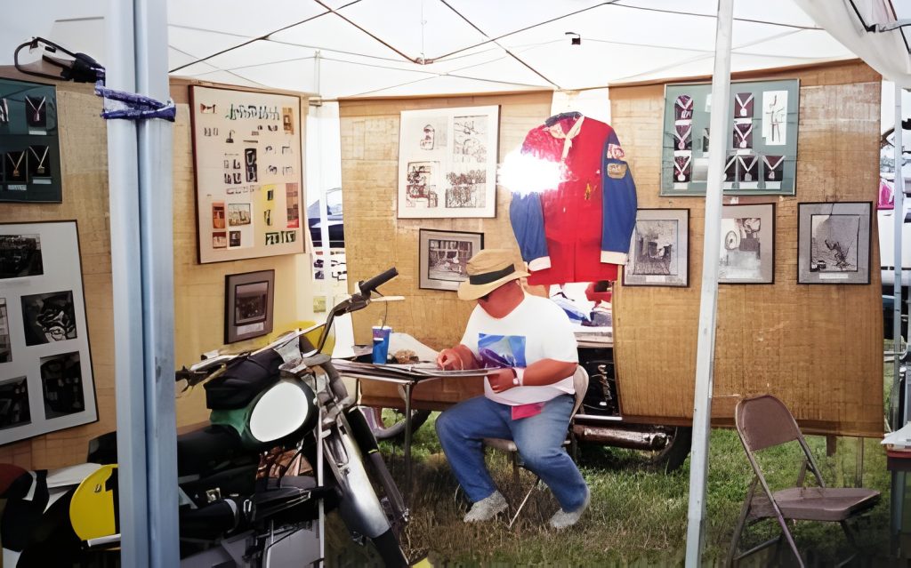 Person sitting at vintage motorcycle show booth.