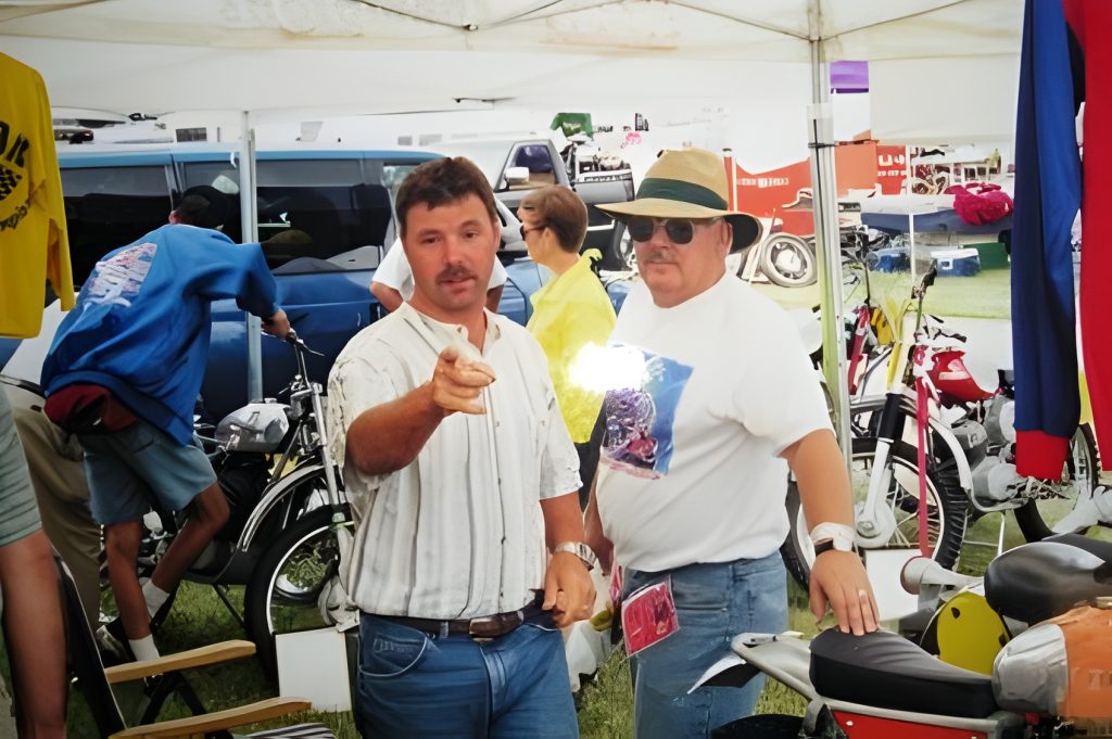 Men discussing motorcycles under a tent.