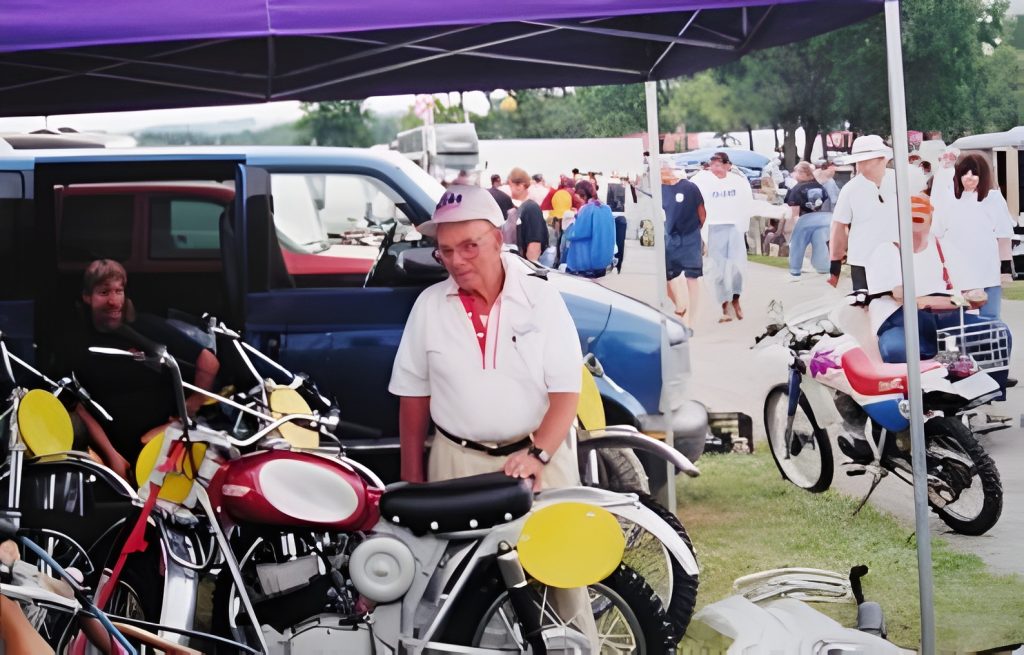 Older man with motorcycles at outdoor event.