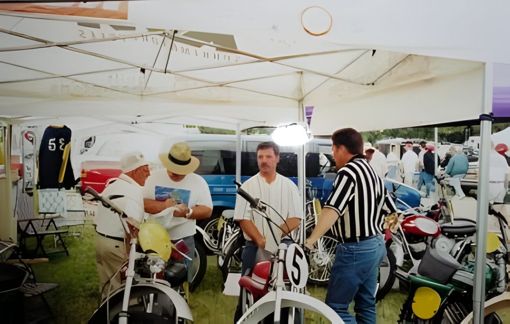 People at vintage motorcycle event under canopy tent.