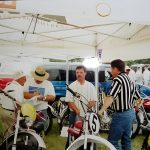 People at vintage motorcycle event under canopy tent.