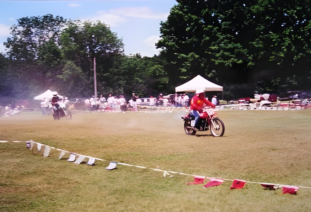 Motorcyclists racing on grassy field with spectators