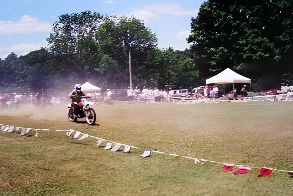 Motorcyclist racing on grassy field under blue sky.
