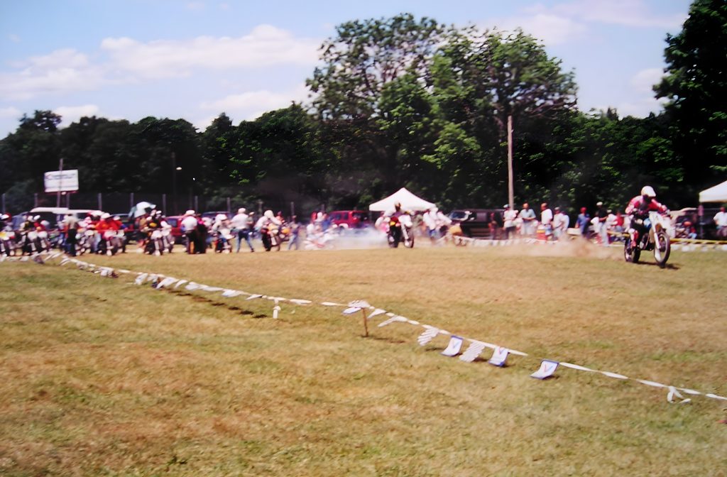Motorcycle race on grassy field with spectators watching.