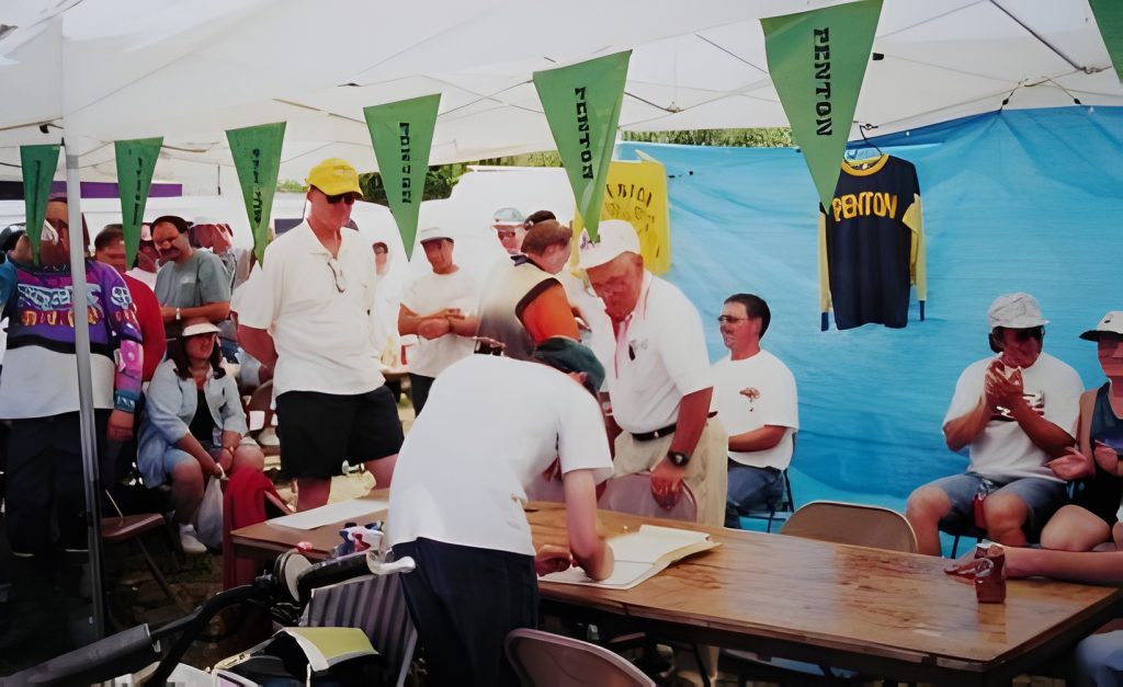 Group gathering under tent with banners and jersey.