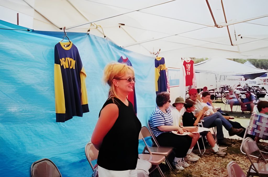 Woman in black shirt at outdoor event with jerseys.