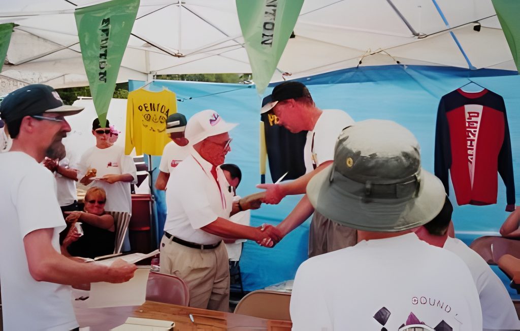 People shaking hands at outdoor event under canopy.