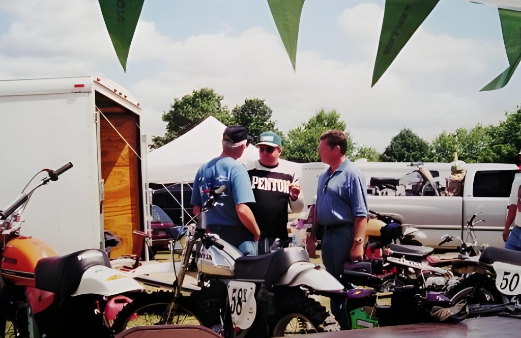 Three men discussing near motorcycles outdoors.