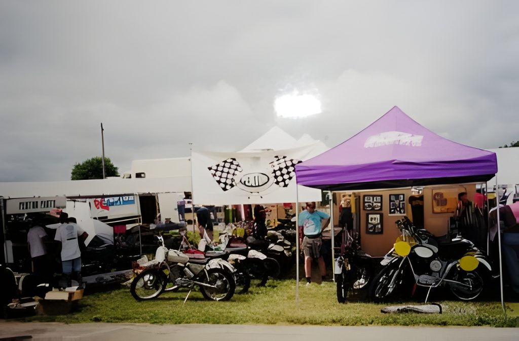 Vintage motorcycles under event tents on grassy field.