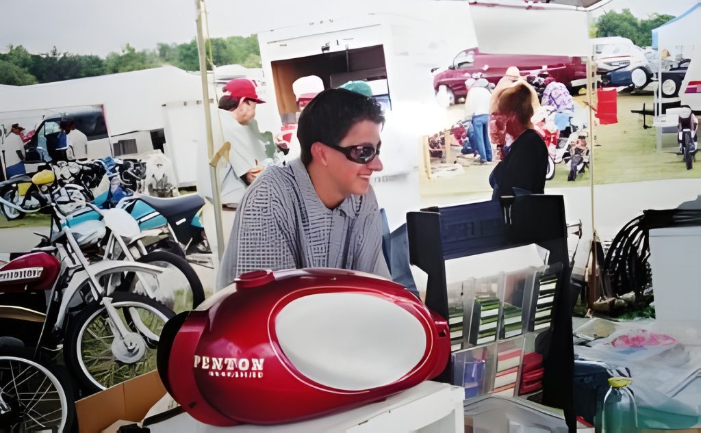 Man selling motorcycle tanks at outdoor market.