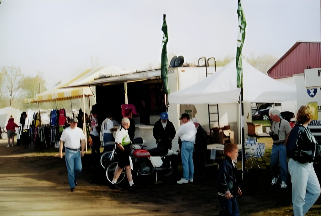 People exploring outdoor market stalls, various items on display.