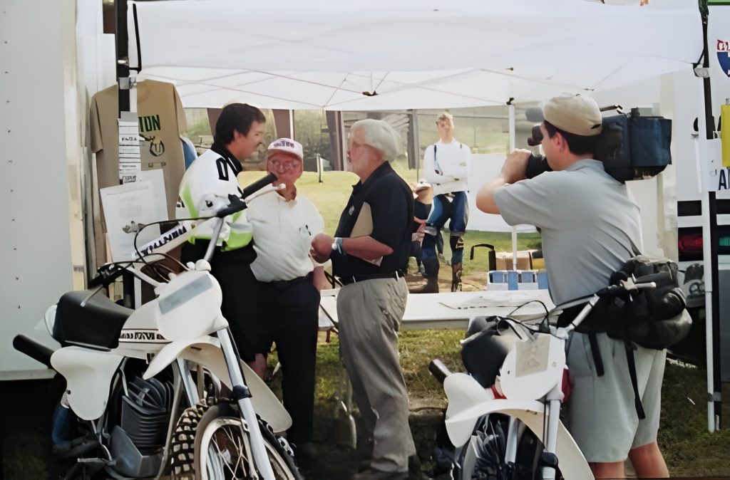 People conversing next to motorcycles, filmed by cameraman.