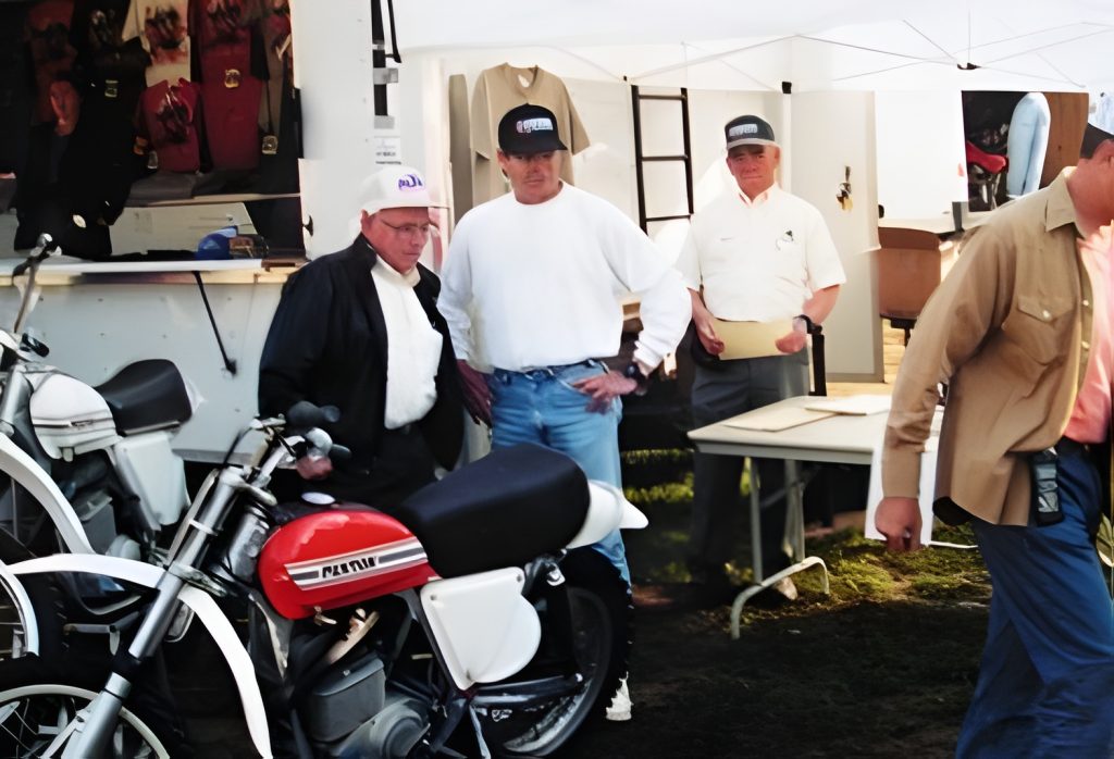 Men examining classic motorcycles at outdoor event.