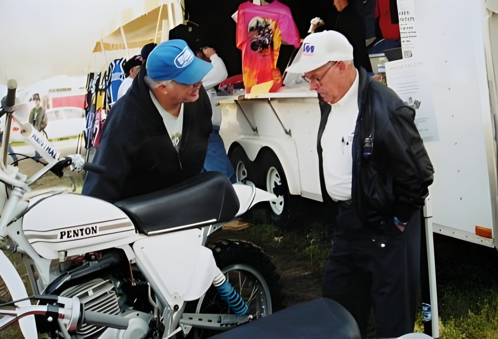 Two men talk beside a classic Penton motorcycle.