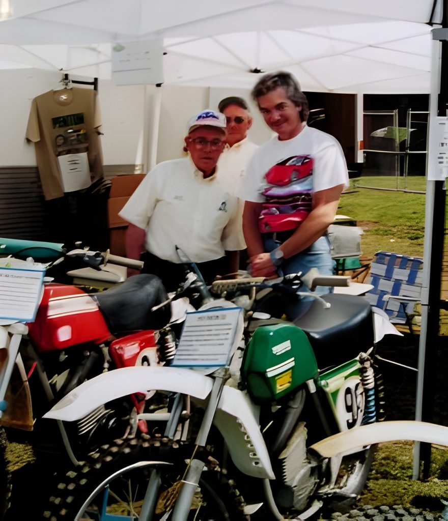 People posing with vintage motorcycles at outdoor event.