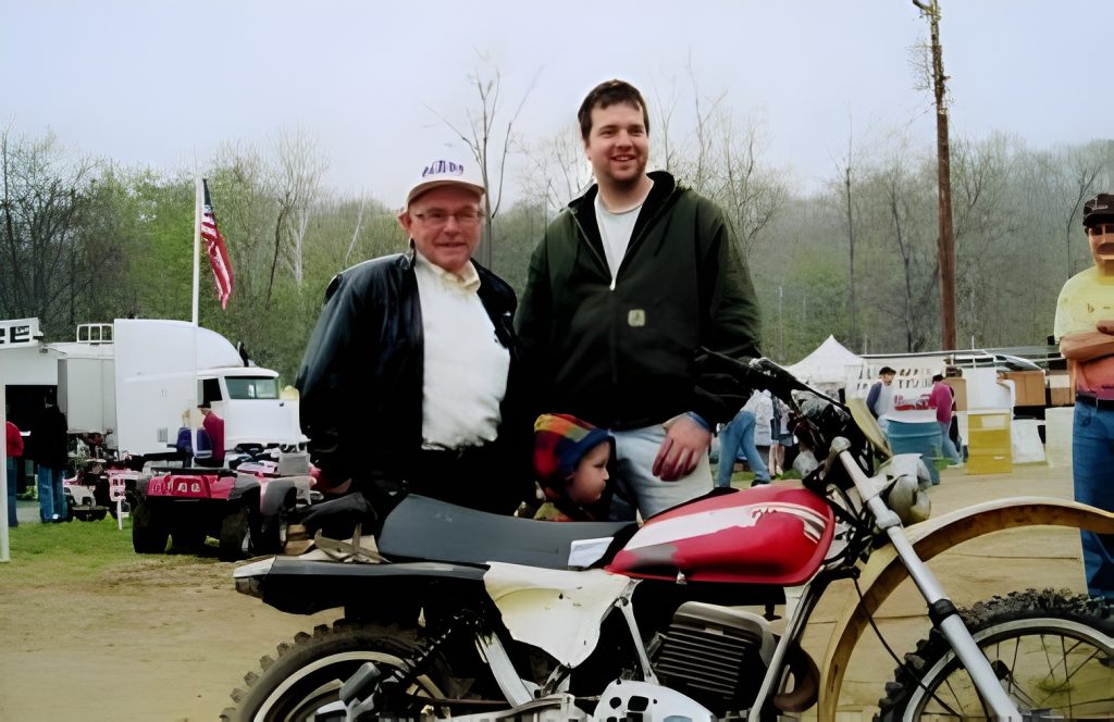 Two men and child with vintage motorcycle at event.