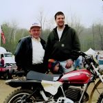 Two men and child with vintage motorcycle at event.