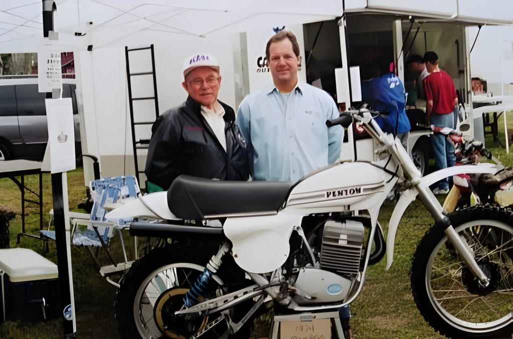 Two men standing by a vintage motorcycle display.