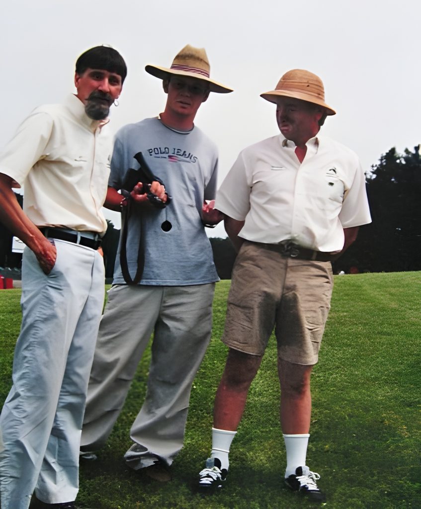 Three men in hats standing on a grassy field.