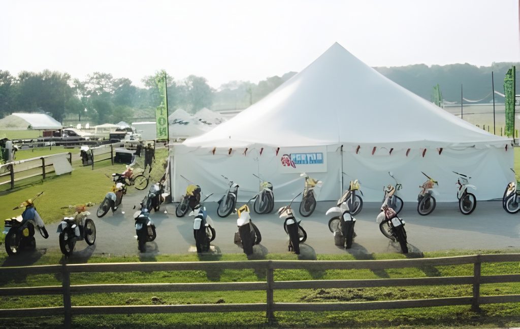 Motorcycles displayed outside white tent in field.