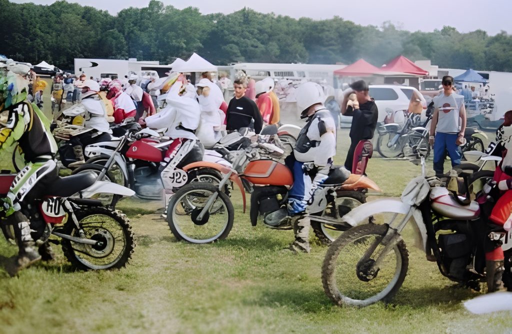 Motorcyclists gathered at outdoor event with trees nearby.