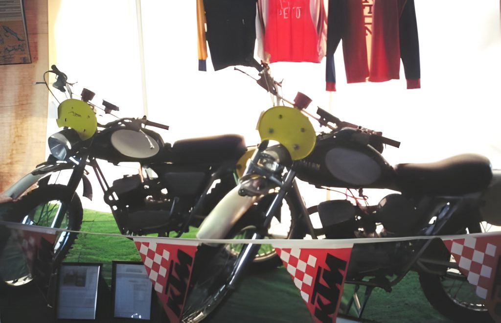 Two vintage motorcycles displayed with racing flags.