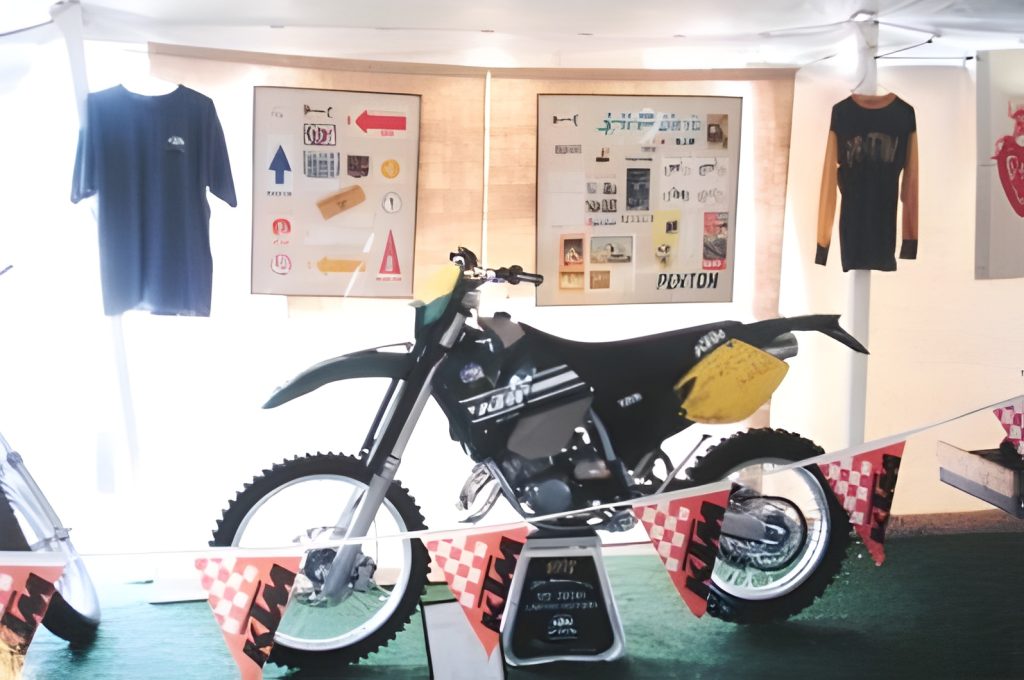 Motorcycle display with shirts and artwork in background.