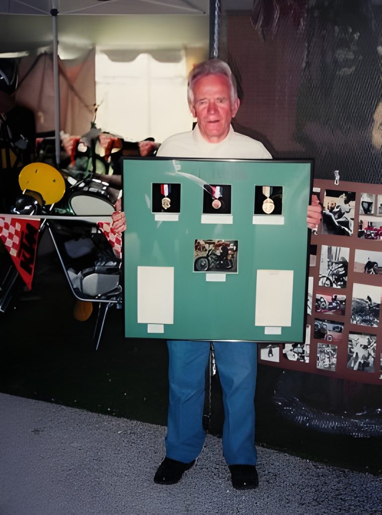 Man holding framed awards and memorabilia display.